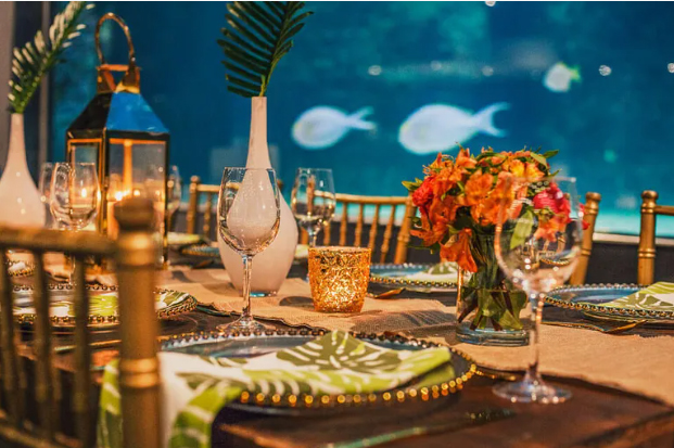 Elegant gala dinner table setting at the Two Oceans Aquarium featuring floral centrepieces, candlelight and ocean backdrop in preparation for a charity fundraising event.