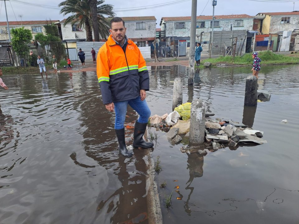Councillor Rob Quintas stands in flooded street in Parkwood, Cape Town, inspecting stormwater drainage impact after heavy rainfall affected residential communities.