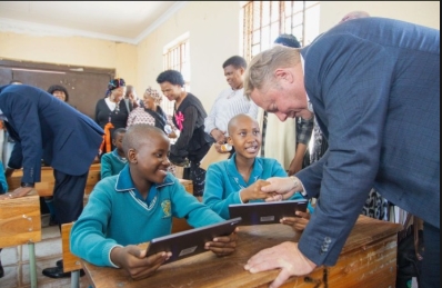Learners in a South African classroom using tablets while interacting with a visitor, highlighting digital learning enabled by school connectivity.