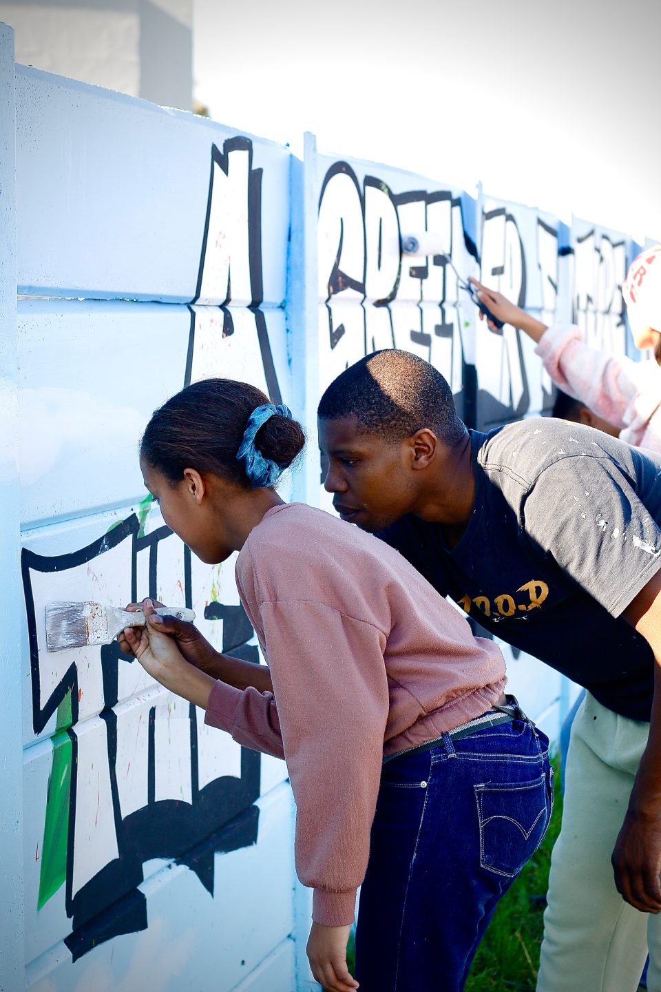 Young community members paint over graffiti-covered walls as part of a youth-led urban beautification and anti-gang initiative in Ravensmead.