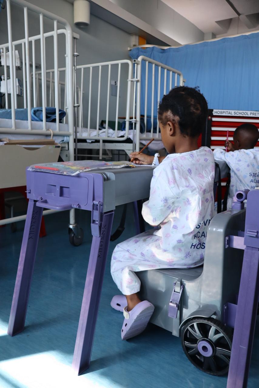 A hospitalised child uses a portable MiDesk study station inside a paediatric hospital ward while continuing schoolwork during medical treatment.