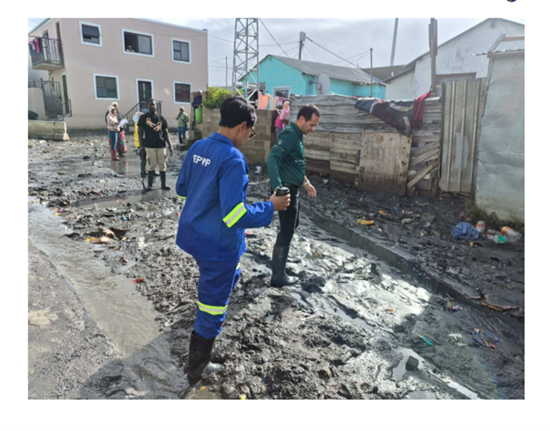 Relief workers and community members walk through a muddy, flood-affected informal settlement in the Western Cape following severe flooding.