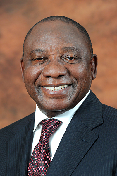 Official portrait of President Cyril Ramaphosa wearing a dark suit, white shirt and patterned red tie against a neutral background.