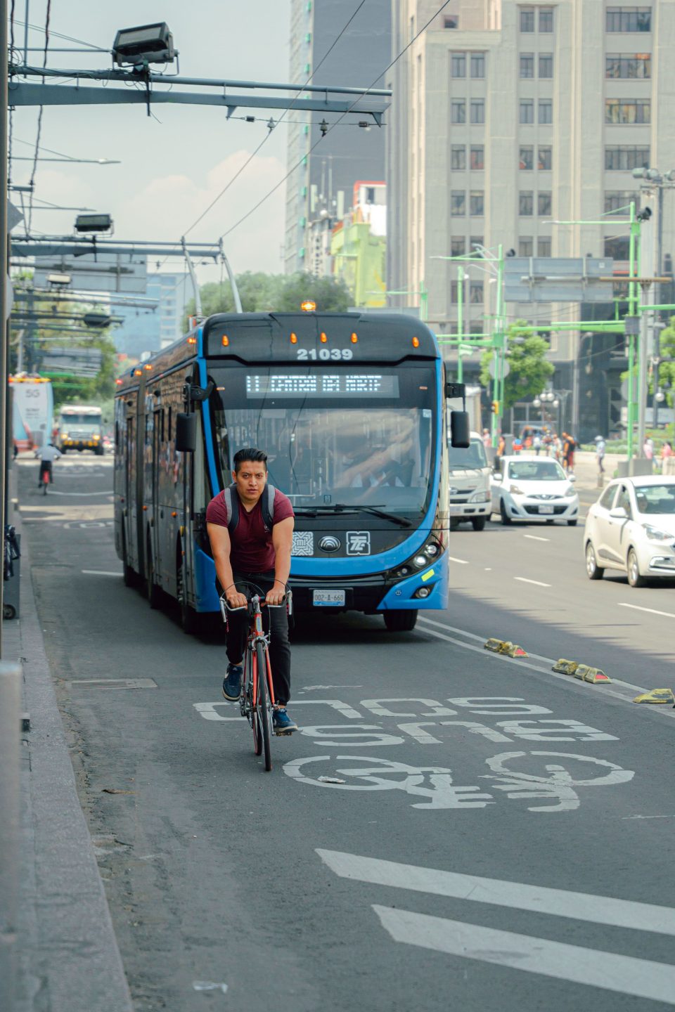 A cyclist rides in a dedicated bike lane alongside a public transport bus in an urban environment, highlighting sustainable transport options.