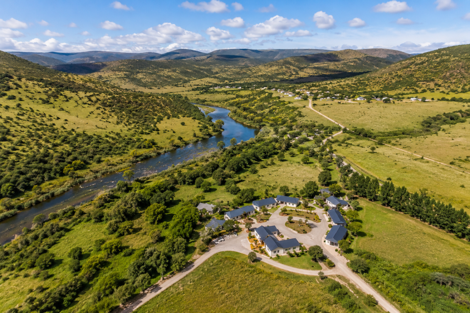 Aerial view of a rural Eastern Cape landscape with green hills, a river, farmland and a tourism lodge surrounded by nature.