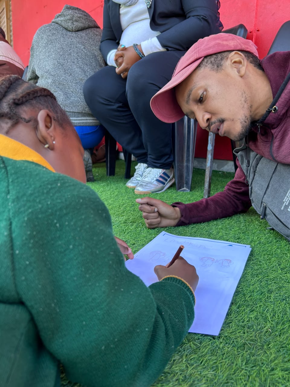 A father participating in Nal'ibali's Mandela Day programme helps a learner with a drawing activity, encouraging creativity, storytelling and literacy at Charles Duna Primary School in Gqeberha.