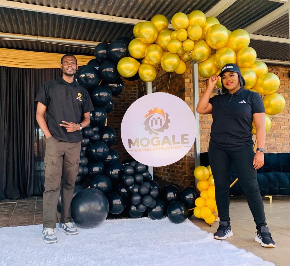 Two participants stand beside Mogale Tailings Retreatment branding during its youth-focused career awareness initiative in the West Rand.