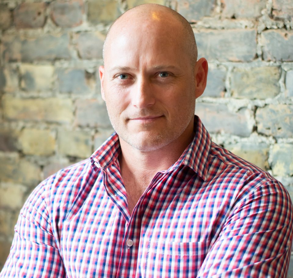 Warren Hickinbotham, Co-Founder of Organic & Natural Products Expo Africa, standing with folded arms in front of a brick wall.