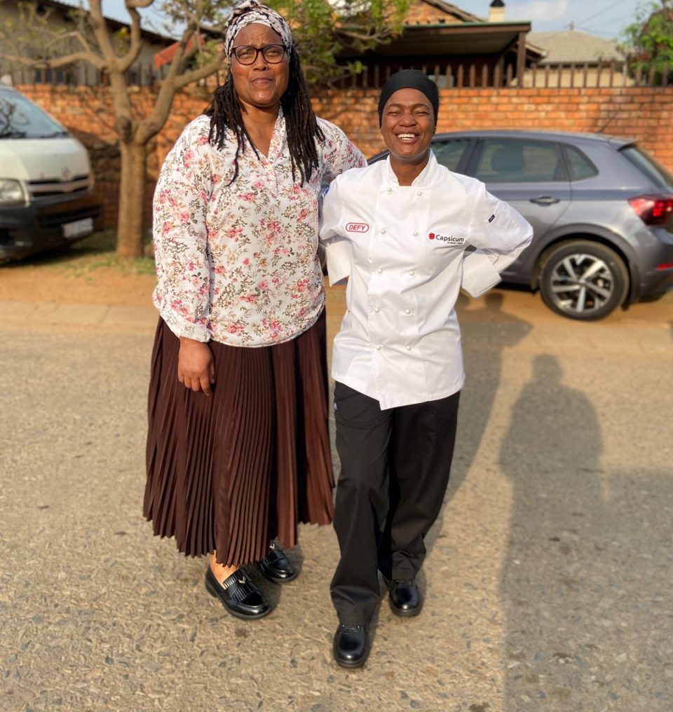 Gogo Nelly Sibanyoni stands alongside her daughter Phindile, who wears her professional chef’s uniform after completing culinary training.