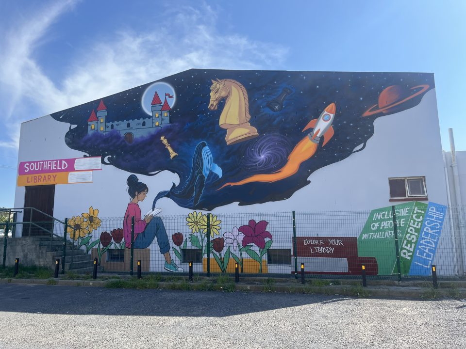 Colourful mural covering the exterior wall of Southfield Library in Cape Town, featuring reading, chess, space, nature and accessibility themes.