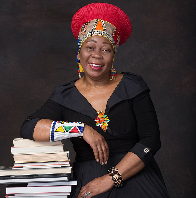 Dr Gcina Mhlophe pictured alongside a collection of books, reflecting her decades-long contribution to South African storytelling, literature and cultural heritage.