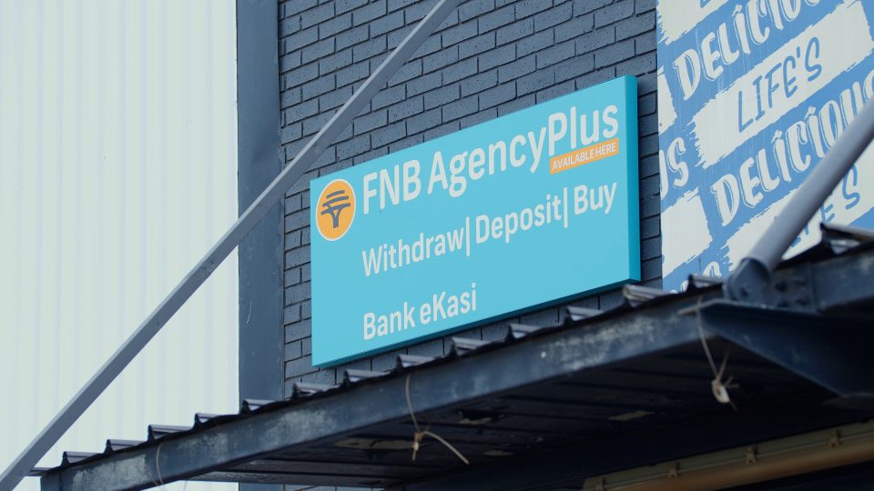 FNB AgencyPlus banking sign displayed outside a local community business offering cash withdrawals and deposits.